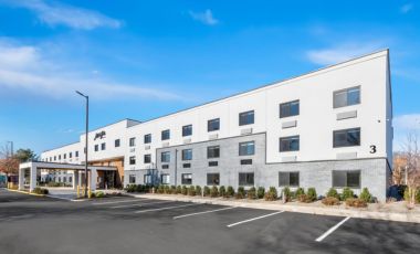 parking Modern multi-story hotel building with white and grey siding under a clear blue sky.