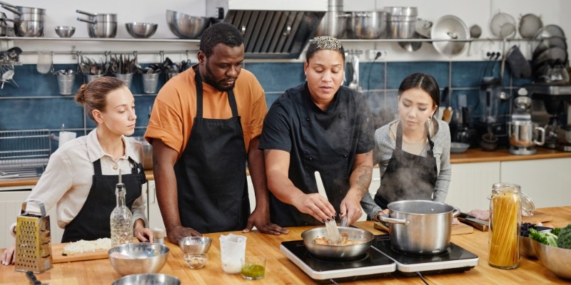 A group of people in a kitchen engaged in food preparation during a cooking class at Jersey Shore culinary workshop.