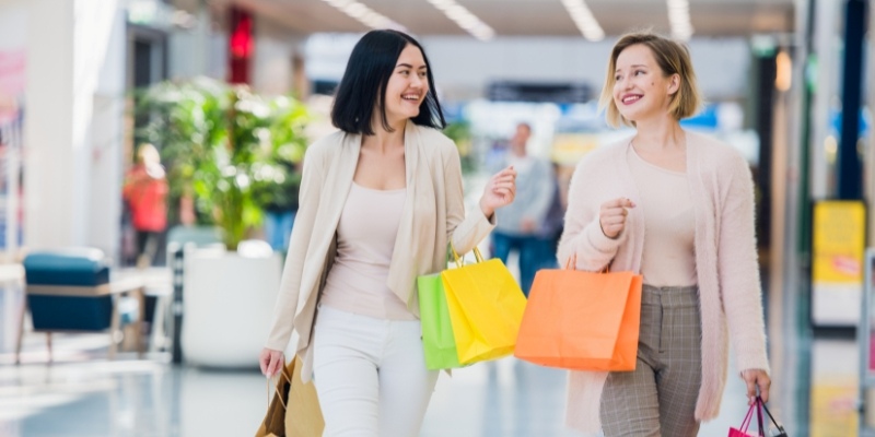 Inside Jersey Shore Premium Outlets, two women walk together, each holding shopping bags filled with their purchases.