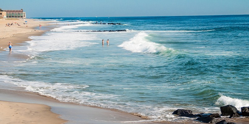 People relax on Asbury Park Beach, featuring a white sand and good weather.