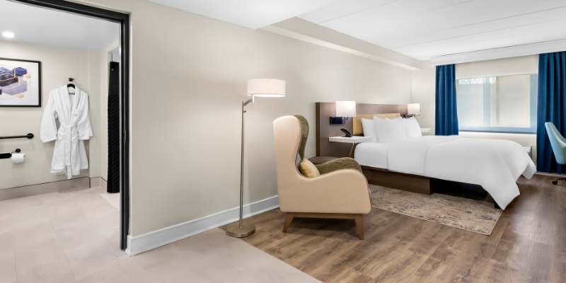 A luxurious hotel room featuring a comfortable bed, elegant chair, and a stylish desk at Latitude Suites, near New Jersey Shore.