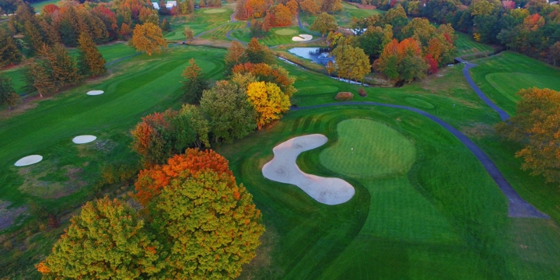 Aerial view of Jumping Brook Country Club, showcasing a golf course with lush green grass and surrounding trees.