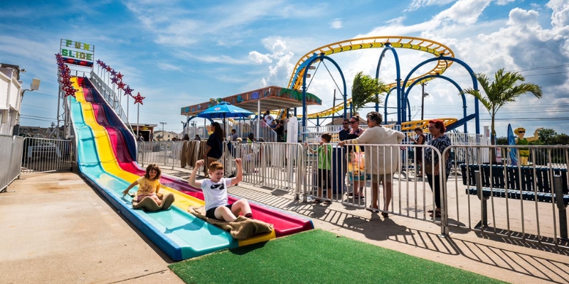 A family experiences fun on the vibrant rainbow slide at Jenkinson’s Boardwalk, surrounded by the beach atmosphere.