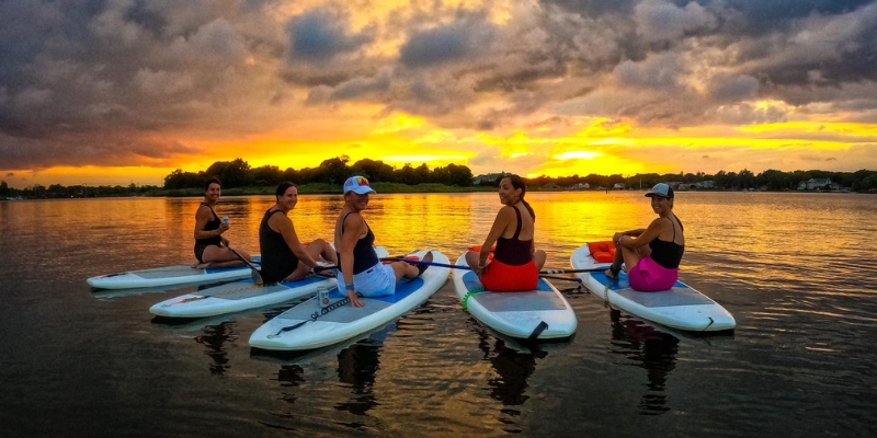 Four people enjoy paddle boarding on calm water at sunset, showcasing outdoor activities at Oceanport Paddle Club, Jersey Shore.
