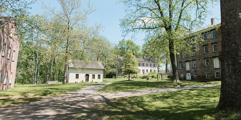 Scenic view of old brick buildings surrounded by trees in Allaire State Park, Tinton Falls, NJ, reflecting local heritage.