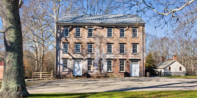 The old brick house, framed by lush trees, highlights the picturesque setting of Allaire Village in Tinton Falls, NJ.
