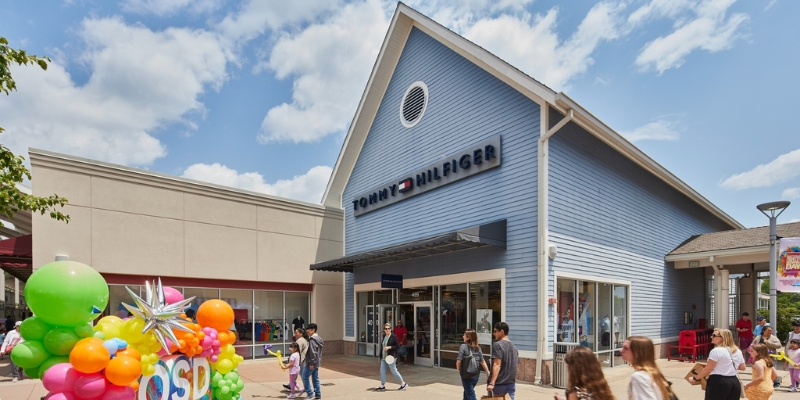 A lively scene of shoppers passing a store decorated with balloons at Jersey Shore Premium Outlets in Tinton Falls, NJ.