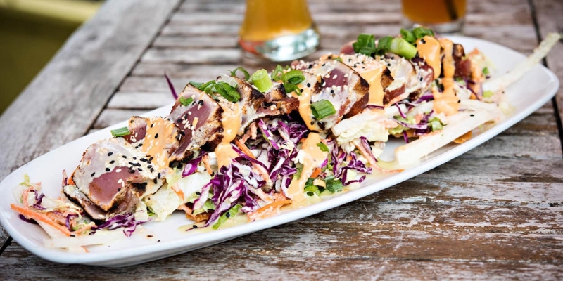 A colorful salad served on a plate with a beer, highlighting a dining experience at Woody’s Ocean Grille near Tinton Falls, NJ.