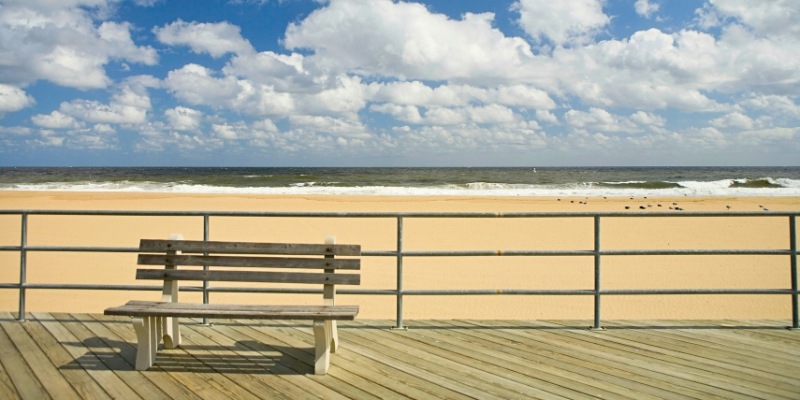 A wooden bench on a boardwalk with a view of the ocean at Asbury Park Beach.