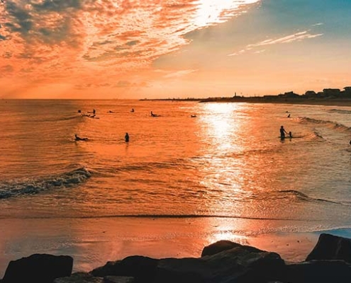 People enjoying a beach sunset in Cape May, New Jersey, with colorful skies and calm ocean waves.