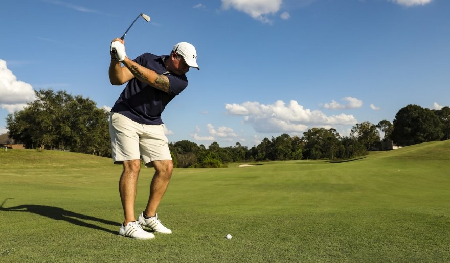 A man in a white hat and black shirt swings a golf club at Bella Vista Country Club, Jersey Shore Golf Courses.