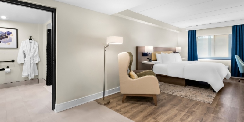 A hotel room featuring a bed, chair, and bathroom, designed for extended stays at Latitude Suites.