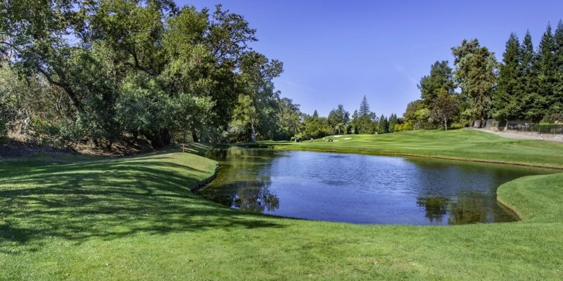 A scenic view of Trump National Golf Club featuring a golf course, a pond, and surrounding trees at Jersey Shore.