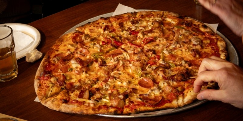 A delicious pizza topped with meat and vegetables, displayed on a table at Mix Lounge & Food Bar near Monmouth University.