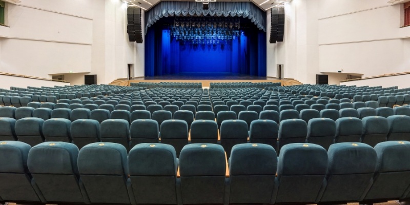 Interior of an empty theater with blue seating and a stage, part of the Pollak Theatre.