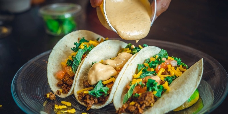 A person pours sauce over three tacos, showcasing a delicious meal at Surf Taco near Monmouth University.