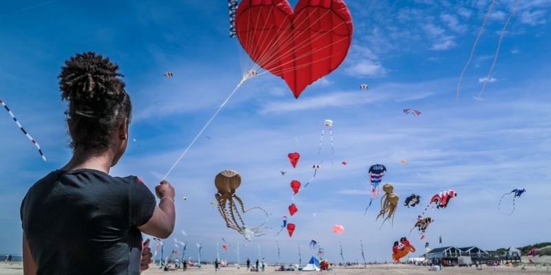 A woman enjoying a sunny day at the beach, flying a kite during the Belmar Kite Festival at the Jersey Shore in spring.
