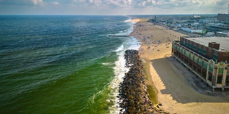 A vibrant beach scene at Asbury Park, with a prominent building adjacent to a large body of water under clear skies.