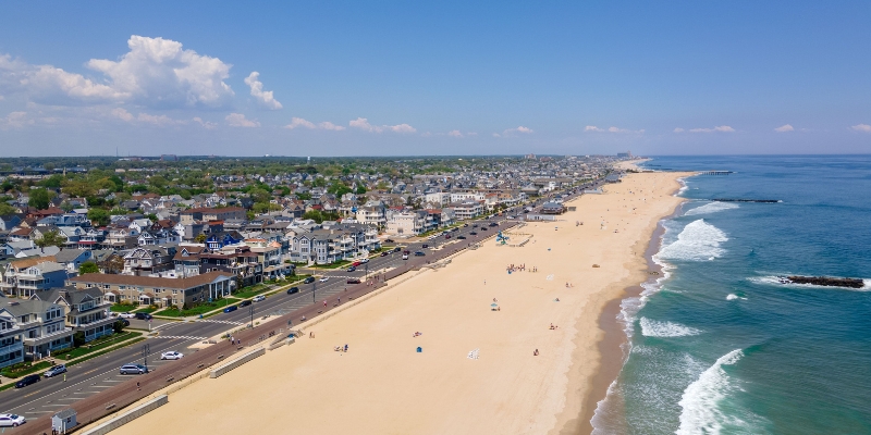 Aerial view of Belmar beach town, showcasing sandy shores and colorful houses under a clear summer sky.