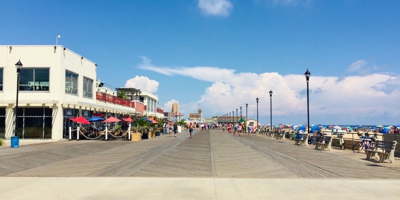 A vibrant Jersey Shore boardwalk scene featuring people walking and colorful umbrellas, evoking a cheerful summer atmosphere.
