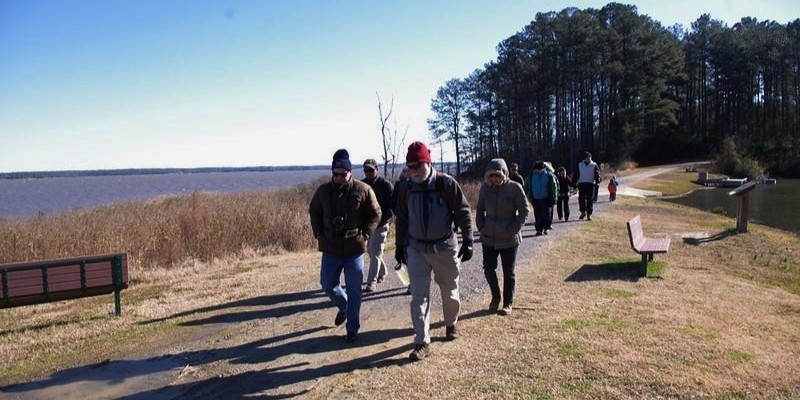 A group of people strolls along a scenic path beside the water, enjoying outdoor activities at the Jersey Shore.