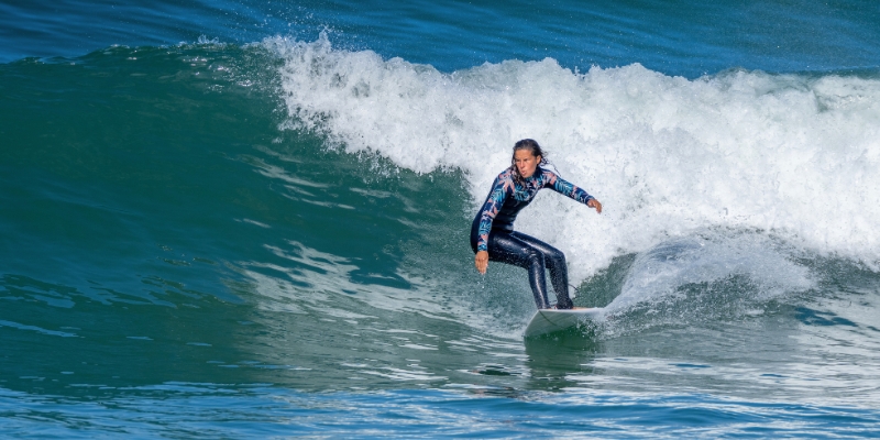 A woman in a wetsuit skillfully rides a wave on her surfboard, showcasing water sports in New Jersey during August.