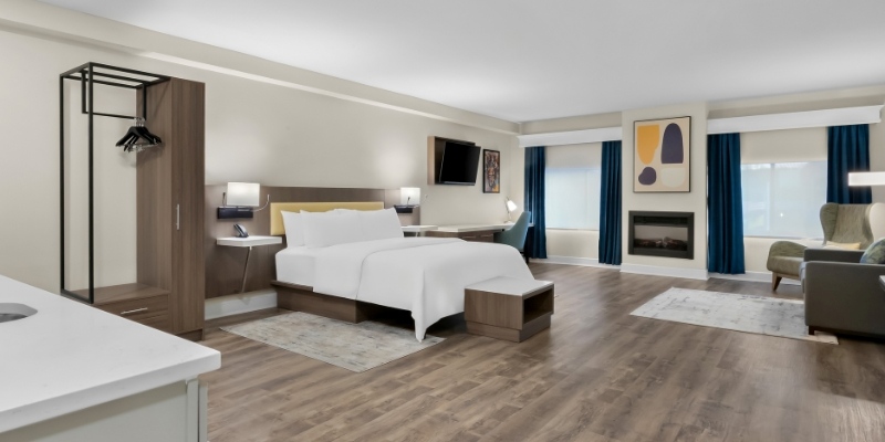 Hotel room featuring a bed, desk, and television, promoting Latitude Suites for August activities in New Jersey.