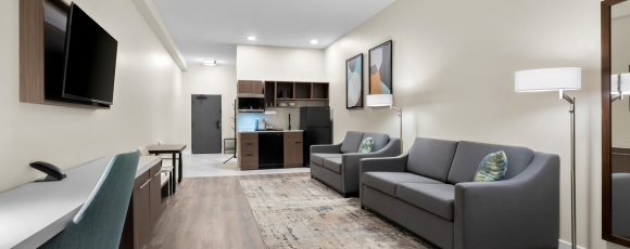 Hotel room featuring a couch, television, and kitchen, promoting exclusive offers near Stone Pony.
