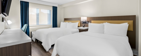 Two beds in a hotel room with a television, promoting group bookings near the Stone Pony.