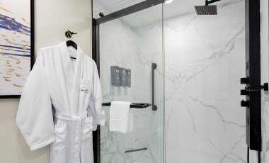A plush white robe hanging on a shower door at Hotel Tinton Falls, NJ, inviting relaxation and comfort.