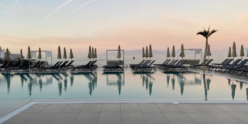 A serene poolside at sunset, featuring lounge chairs and umbrellas, showcasing the ambiance of ICONA Diamond Beach.