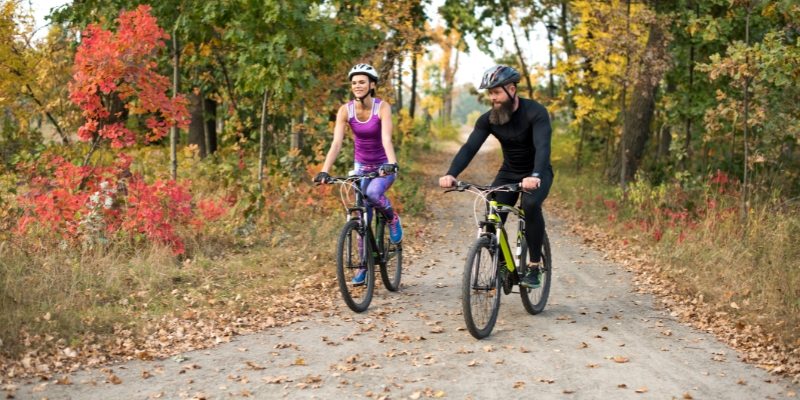 Two individuals cycle on a path amidst vibrant fall colors in New Jersey's autumn landscape.