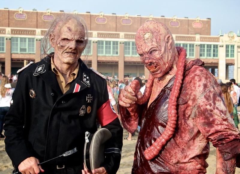 Two men dressed as zombies stand on the beach, promoting the Hotel Near Asbury Park Zombie Walk event.
