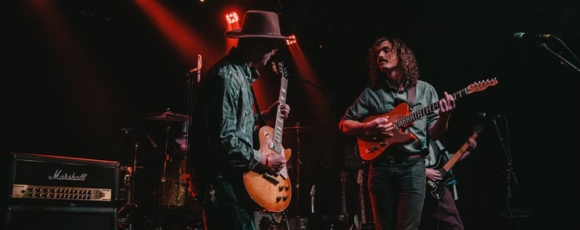 A band performing on stage with guitars at night at the Stone Pony.