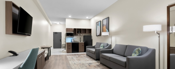 Modern hotel room featuring a couch, television, and kitchen, located near Jersey Shore Premium Outlets for extended stays.