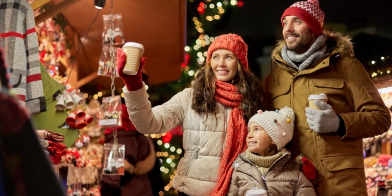 A family enjoys the holiday spirit at a Christmas market in Jersey Shore, with colorful decorations and festive atmosphere around them.
