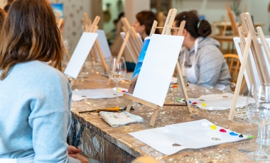 Individuals seated at easels, creating artwork during a community gathering in an event space.