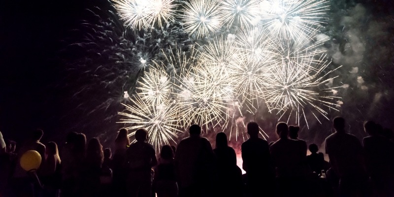A group of people enjoying New Year’s Eve fireworks at Pier Village, illuminated against the dark night sky.