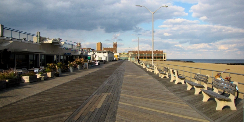 A long wooden boardwalk featuring benches and tables, ideal for relaxation at the Jersey Shore in Asbury Park.