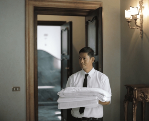 A man in a tie holds a stack of neatly folded towels at a hotel near Bell Works Holmdel.