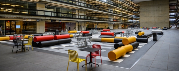 A spacious atrium at Bell Works Holmdel featuring tables and chairs arranged for socializing and work.