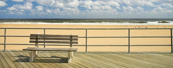 A wooden bench on the boardwalk with a view of the ocean, near a hotel at Jersey Shore, Eatontown, NJ.