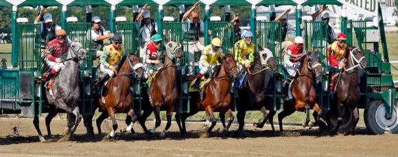 Horses lined up in the starting gate at Monmouth Racetrack, surrounded by excited fans and vibrant decorations.