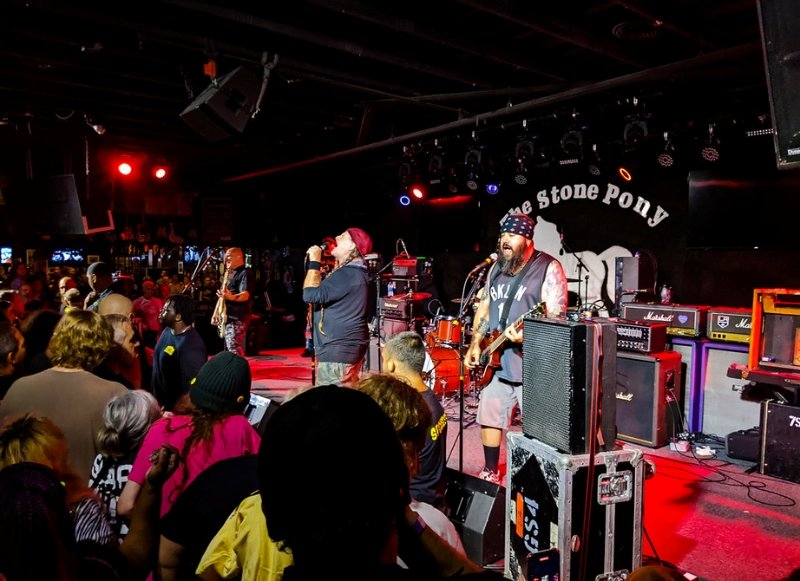 A live band plays on stage at a concert, with an engaged crowd watching at the Stone Pony.