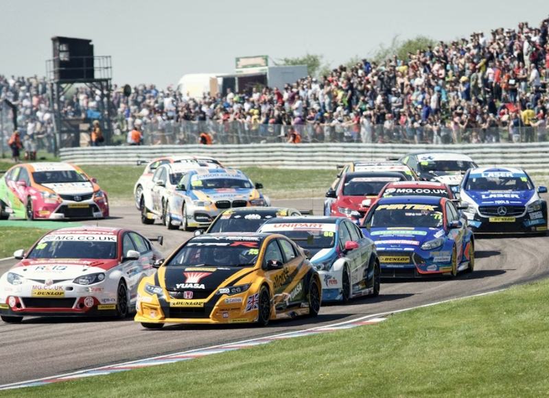Hotel-Near-Wall-Stadium-Speedway-1 A group of cars races on a track while a crowd watches from the stands at Wall Stadium Speedway.