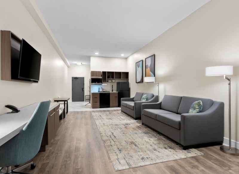 A modern hotel room featuring a couch, desk, and television, located near Bell Works Holmdel.