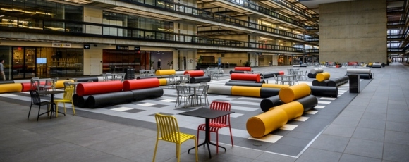 A spacious atrium at Bell Works Holmdel featuring tables and chairs arranged for socializing and work.