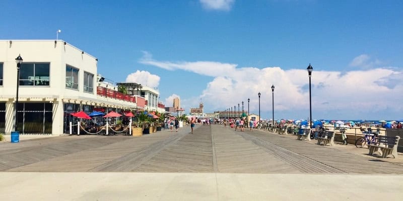 Busy Ocean City Boardwalk with beachgoers, restaurants, and ocean views on a sunny day