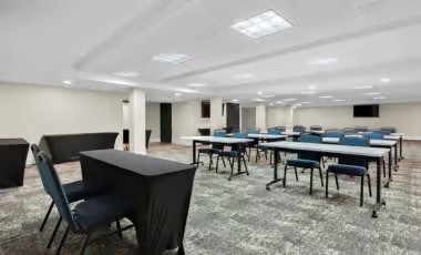 Flexible Event Rooms Spacious corporate training room set up with classroom-style tables and blue chairs.