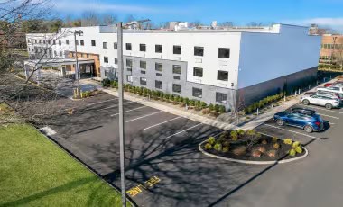 Free Self-Parking Exterior view of the modern, three-story Latitude Suites building and parking lot on a sunny day.